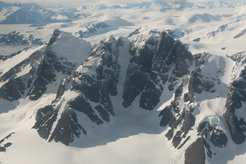 Luftbild eines Bergmassivs mit einem Talkessel im Vordergrund, hinter dem Berg erstrecken sich Gletscher bis zum Horizont.