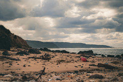 Verlassener Strand mit verstreutem Müll, Felsen unter bewölktem Himmel.